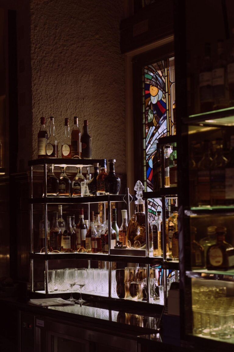 An atmospheric bar scene showcasing a variety of liquor bottles on display with stained glass backdrop.