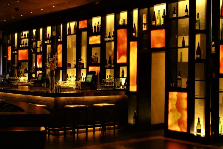 Elegant bar counter with backlit shelves displaying wine bottles and sparkling glassware.