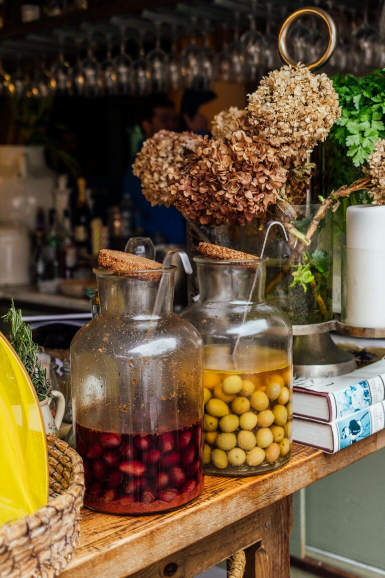 Rustic jars with infused fruits and liquids on a wooden bar, surrounded by dried flowers.